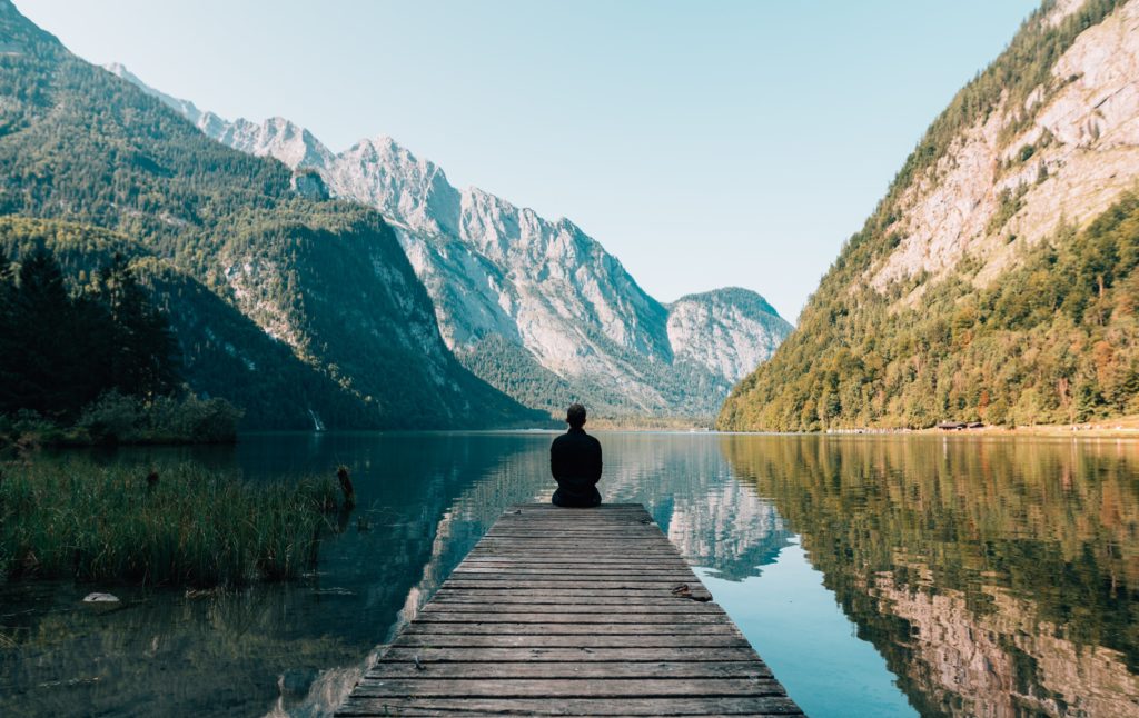 person sitting on a dock looking out at the lake contemplating possibility of post pandemic travel